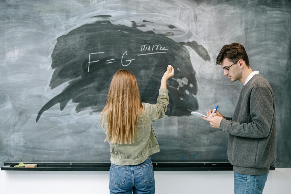 Woman in Gray Long Sleeve Shirt and Blue Denim Jeans Standing in Front of Black Chalk